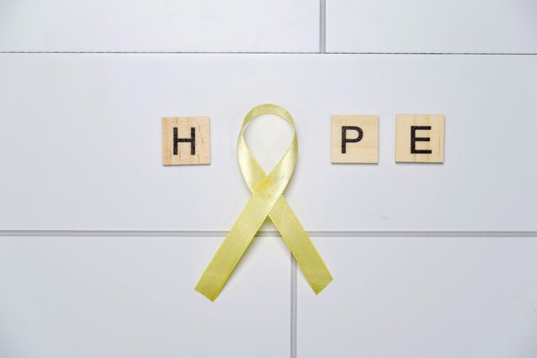 Yellow awareness ribbon forming 'O' with HOPE on tiles, symbolizing support and positivity.