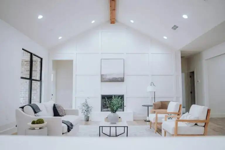 Bright modern living room with high vaulted ceiling, white accent wall, fireplace, and luxury furniture