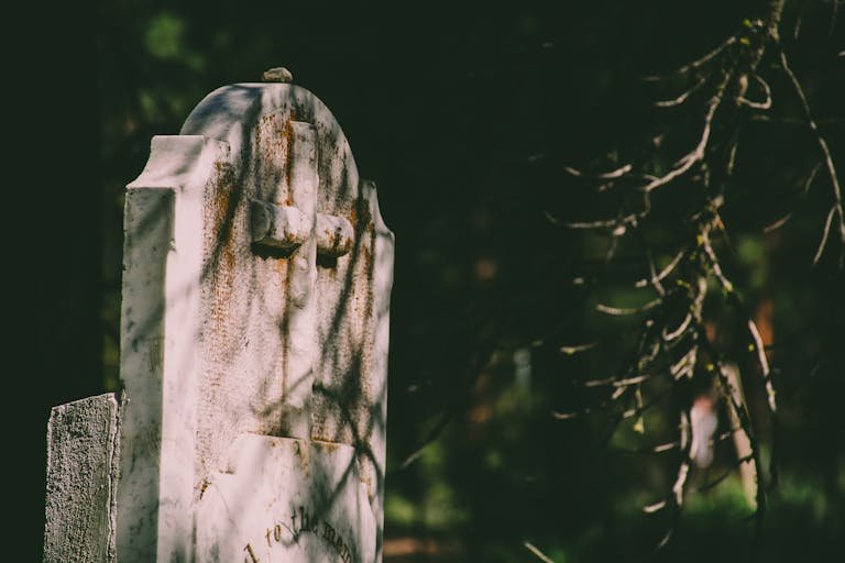 Close-up of a weathered stone tombstone with an engraved cross in a cemetery