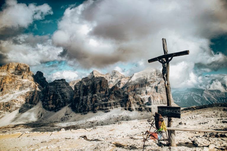 A crucifix silhouetted against dramatic cloudy skies in the Dolomite mountains