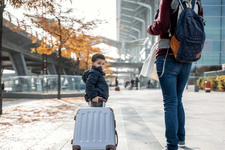 Child pulling a suitcase and looking at the camera while adult standing beside him