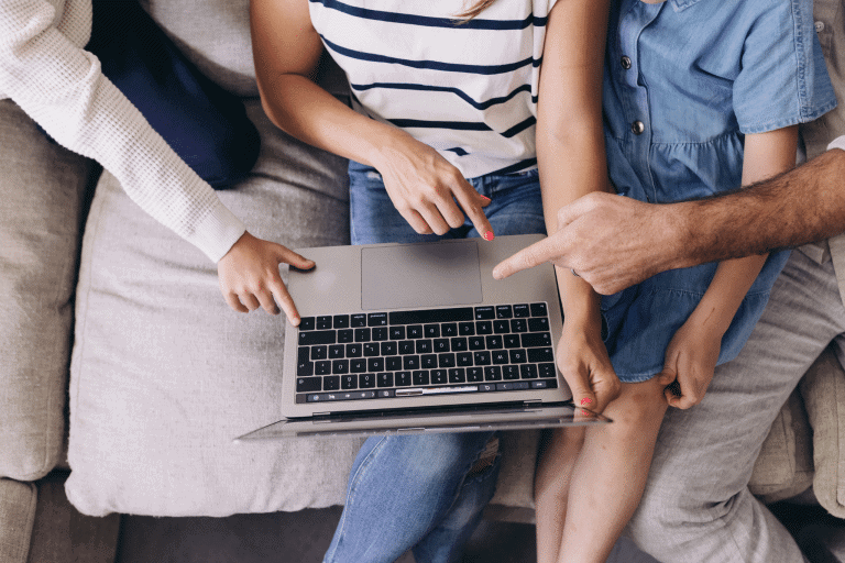 a family planning their vacation on a budget, with hands of parents and child pointing at computer.