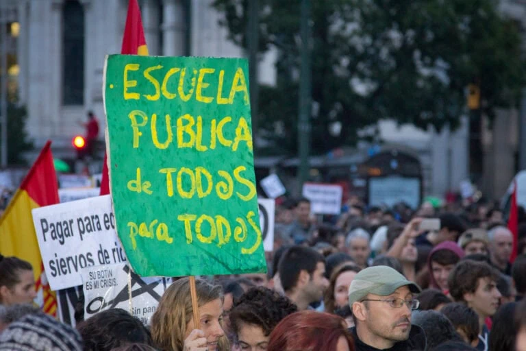Una multitud asiste a una manifestación, sosteniendo carteles en apoyo a la educación pública, entre ellos destaca uno en ama