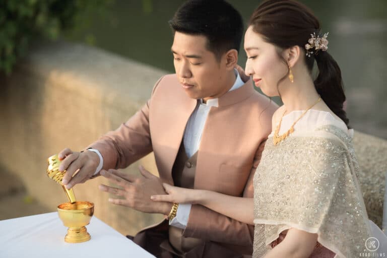 The groom pours water from a small gold vessel to share merit after the monks' blessing, with the bride beside him, at Dusit Thani Hua Hin