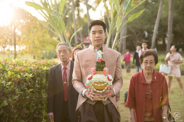 The groom carries the decorated Khan Maak tray between his parents at the start of the procession at Dusit Thani Hua Hin