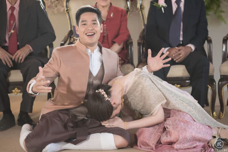The bride bows low beside the laughing groom after the ring exchange at their Thai ceremony at Dusit Thani Hua Hin