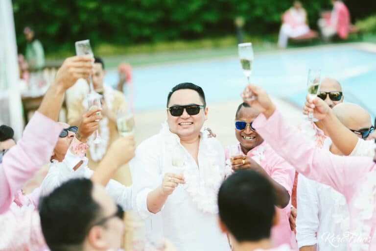 The groom in sunglasses raises a glass with friends at the poolside Mehendi party in Pattaya