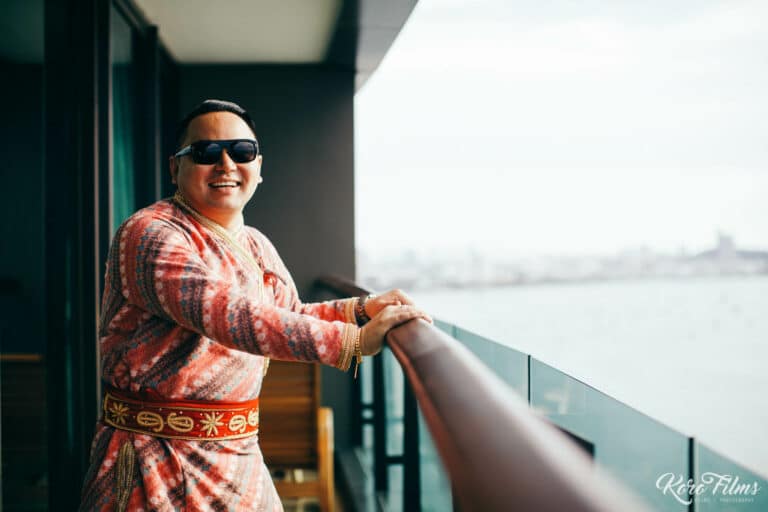 The groom in his red wedding outfit on a hotel balcony overlooking the sea in Pattaya