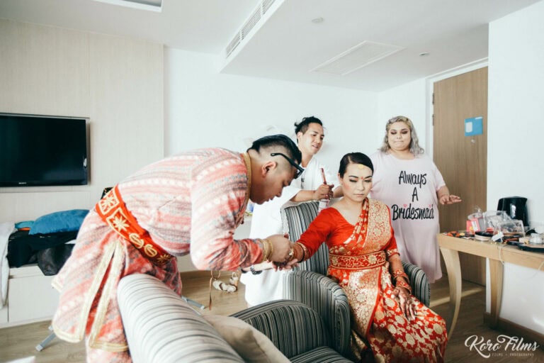 The groom leans in to the seated bride in her red sari while a bridesmaid watches, Pattaya