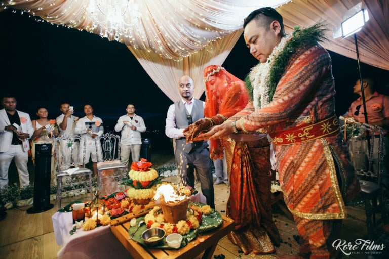 The groom leads the veiled bride around the sacred fire under the mandap at night in Pattaya