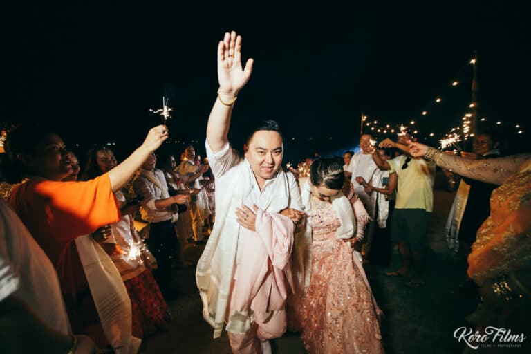 The groom raises his hand as guests dance with the couple at the beach reception in Pattaya