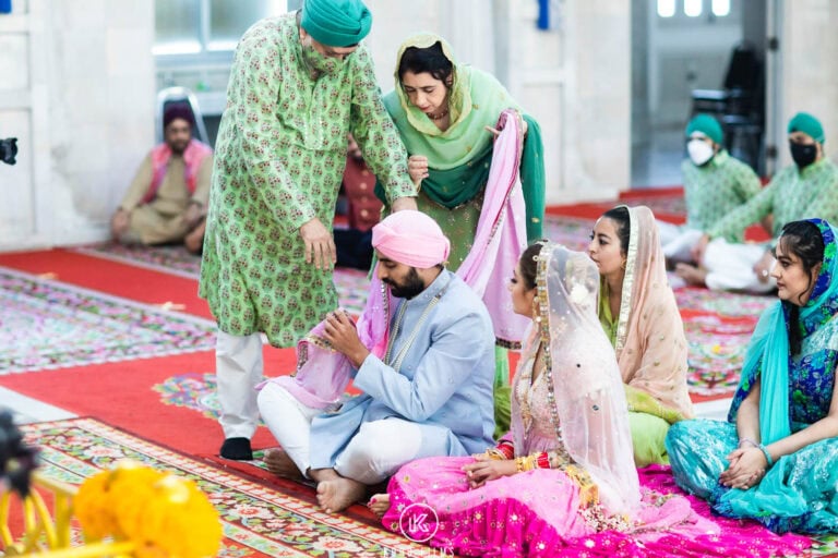 An elder relative blesses the seated Sikh couple in the gurdwara