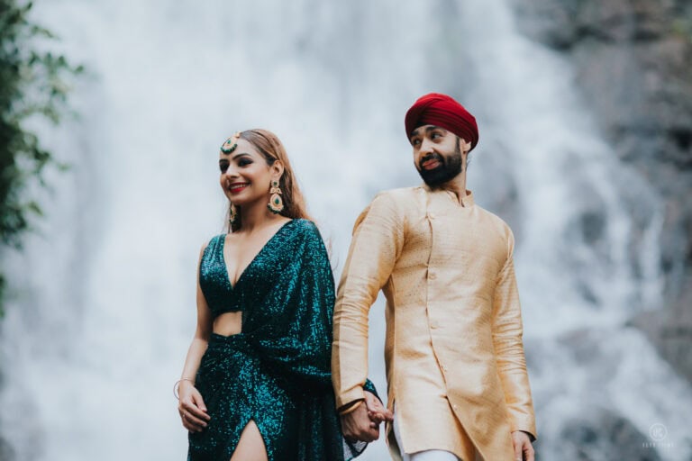 Twinkle in an emerald sari and Dev in a gold sherwani and red turban in front of a waterfall in Nakhon Nayok