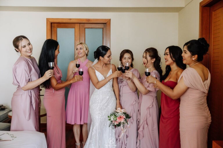 The bride and her bridesmaids in pink dresses raise glasses of red wine before the ceremony at Sheraton Hua Hin