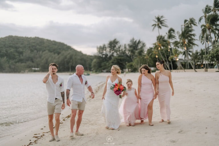 The bride and groom walk along the beach with their bridal party in white and blush at Baan Puri, Koh Samui