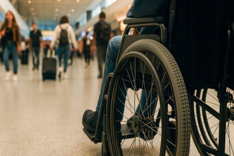 Close-up of a traveler using a wheelchair in a busy airport terminal, highlighting accessible travel and mobility support. Featured image for the blog post '5 Tips to Actually Make Traveling With a Disability Easier'.