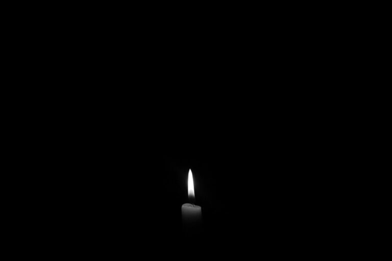 A lit white candle against a black background.