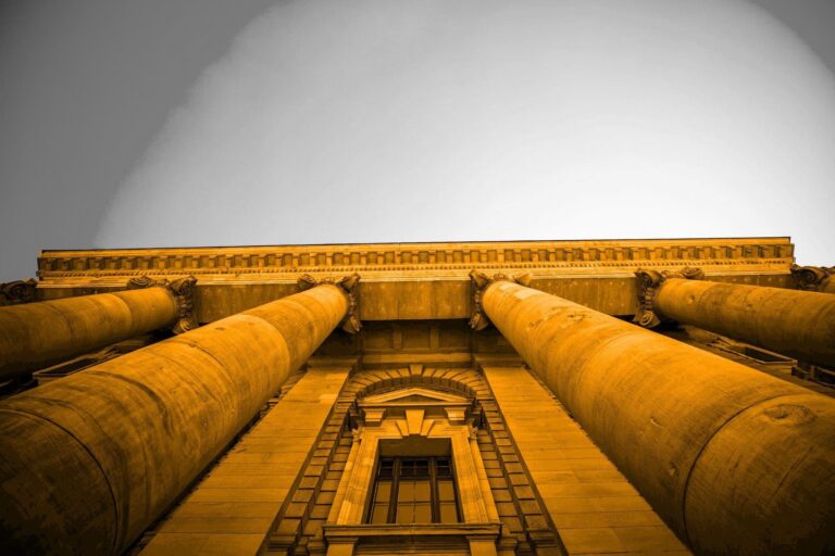 A black and white image of a big building with pillars. The building is orange