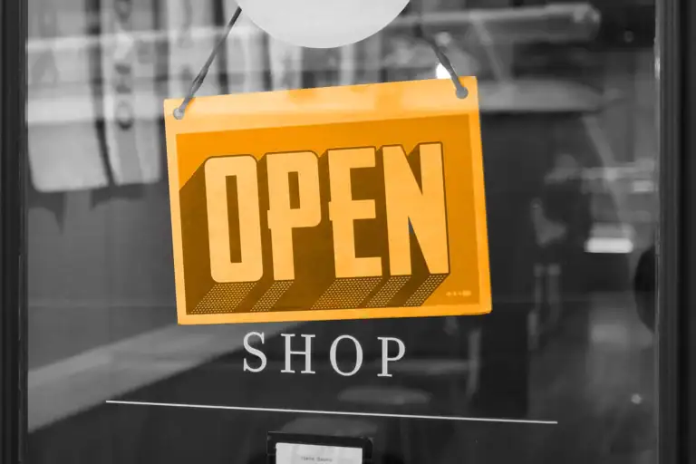 A black and white image of a door, with a orange open sign hanging on the door