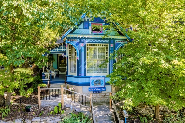 Blue Victorian-style house with intricate trim and lush greenery in Eureka Springs, AR.