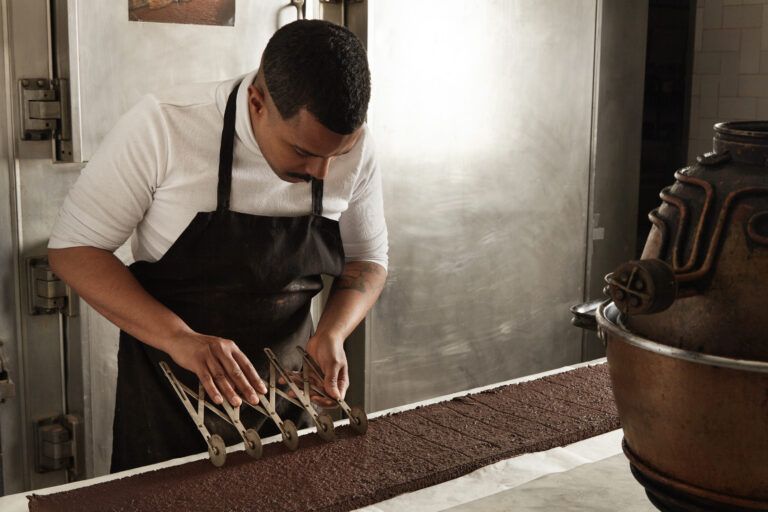 Chocolatier professionnel découpant une tablette de chocolat en portions égales avant l'emballage, processus artisanal Yvoria