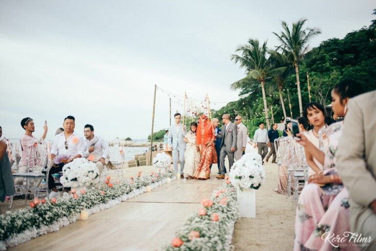 Guests watch the bride arrive along the flower-lined beach aisle at Cape Dara Resort, Pattaya