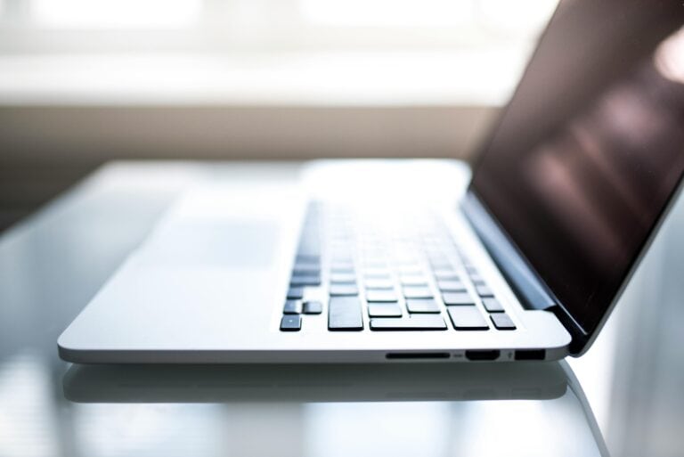 Side view of an open silver laptop on a reflective surface with a blurred bright background.