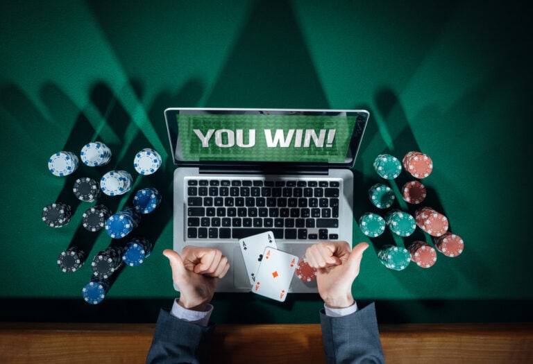 Person sitting in front of a laptop computer with two Aces resting on the trackpad. The computer is surrounded by casino chips. The person is giving two thumbs up.