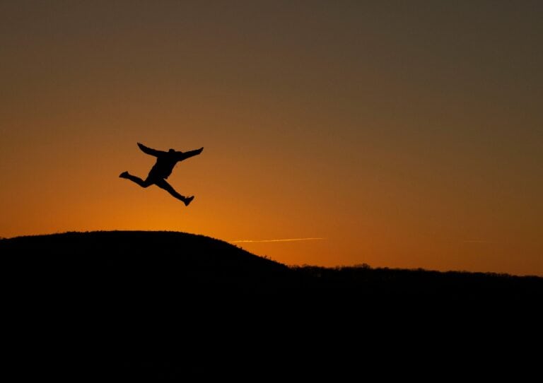 A striking silhouette of a person leaping in front of a vibrant sunset backdrop, symbolizing freedom.