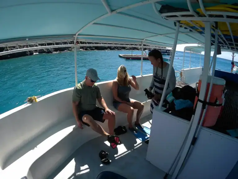 SNUBA guide preparing equipment with first-time guests aboard the boat in clear Little Bay water