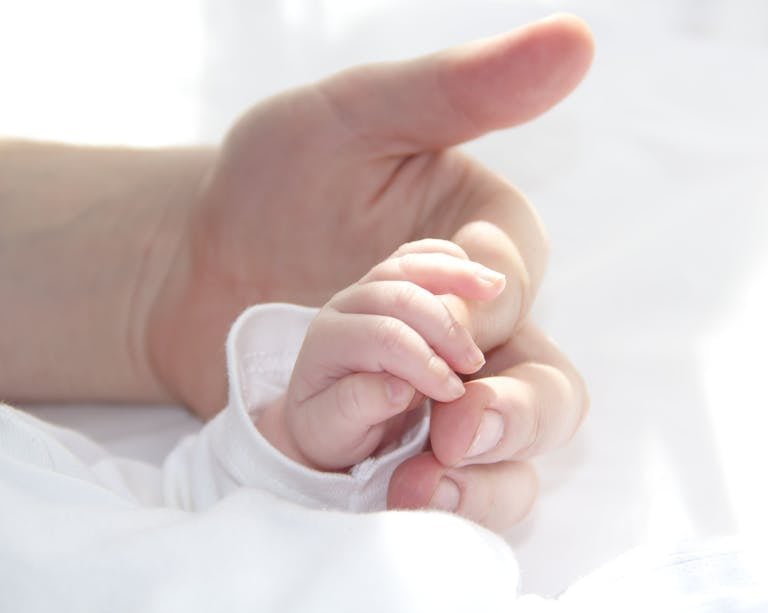 Close-up of a baby hand holding a fathers finger symbolizing the mystery of adoption in Christ