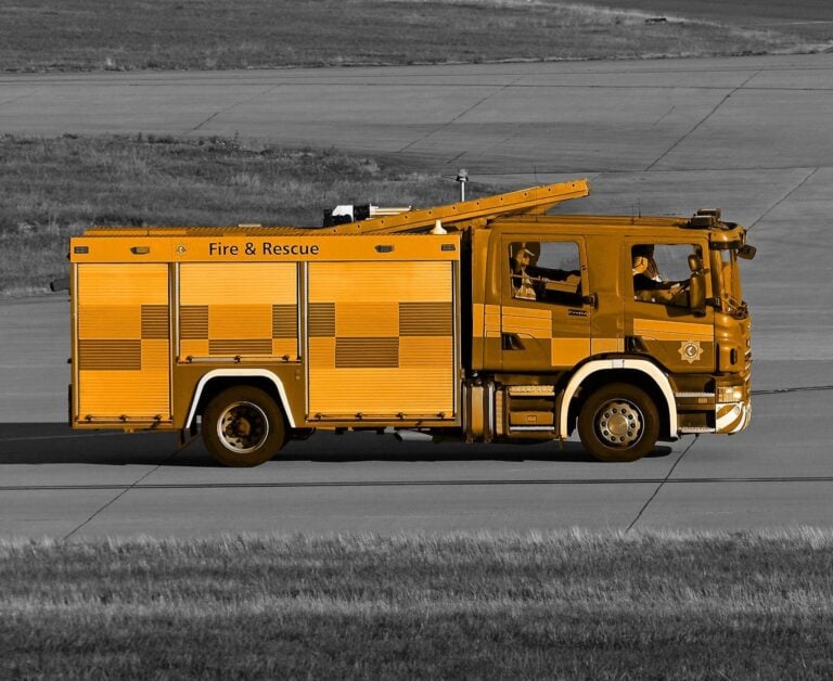 A black ad white image of a road with an orange fire truck driving down it