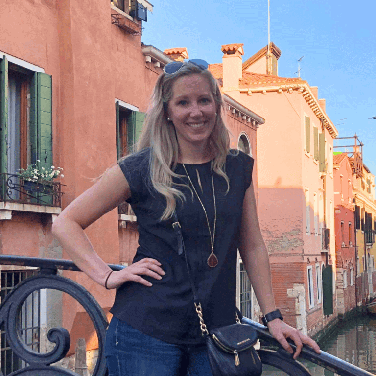 Smiling woman standing by Venice canal with colorful buildings.