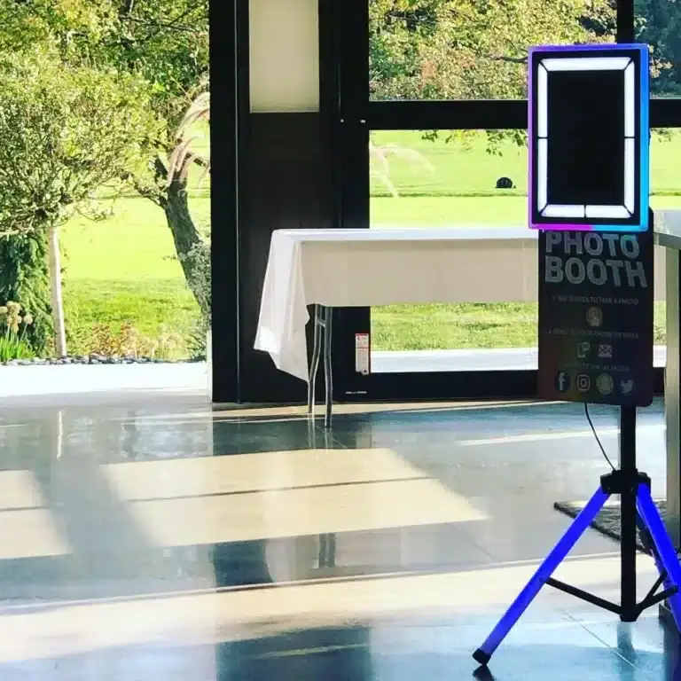 Fastbooth's setup in Grand Rapids, Michigan featuring a modern LED touchscreen display on tripod legs, positioned indoors near large windows with a green outdoor view.
