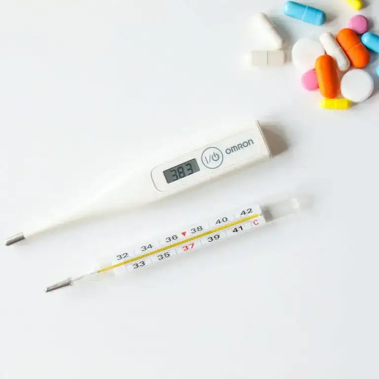 Ein digitales und ein analoges Fieberthermometer neben bunten Tabletten auf weißem Hintergrund.