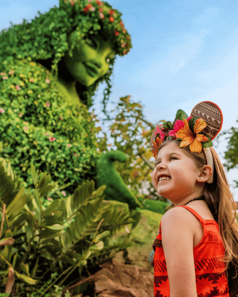Young girl smiling at a green Disney character in a garden setting.