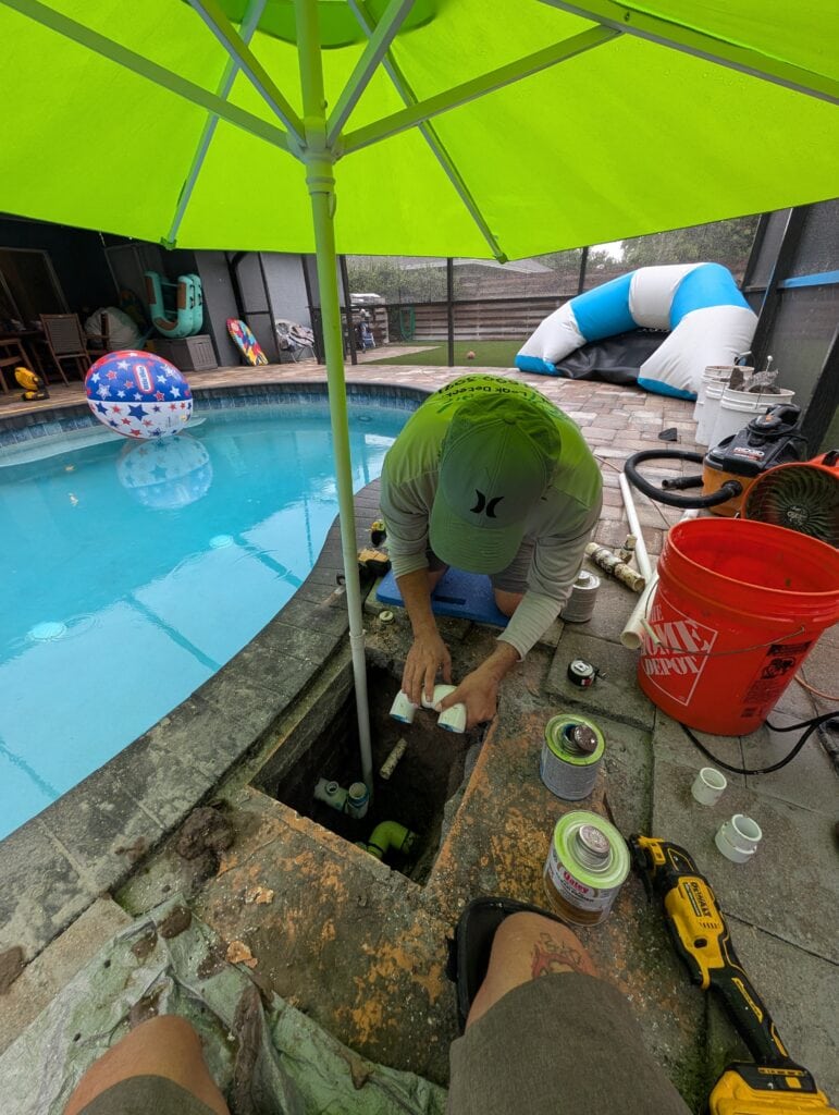 Gluing new PVC fittings during an underground pool plumbing repair through a small deck opening