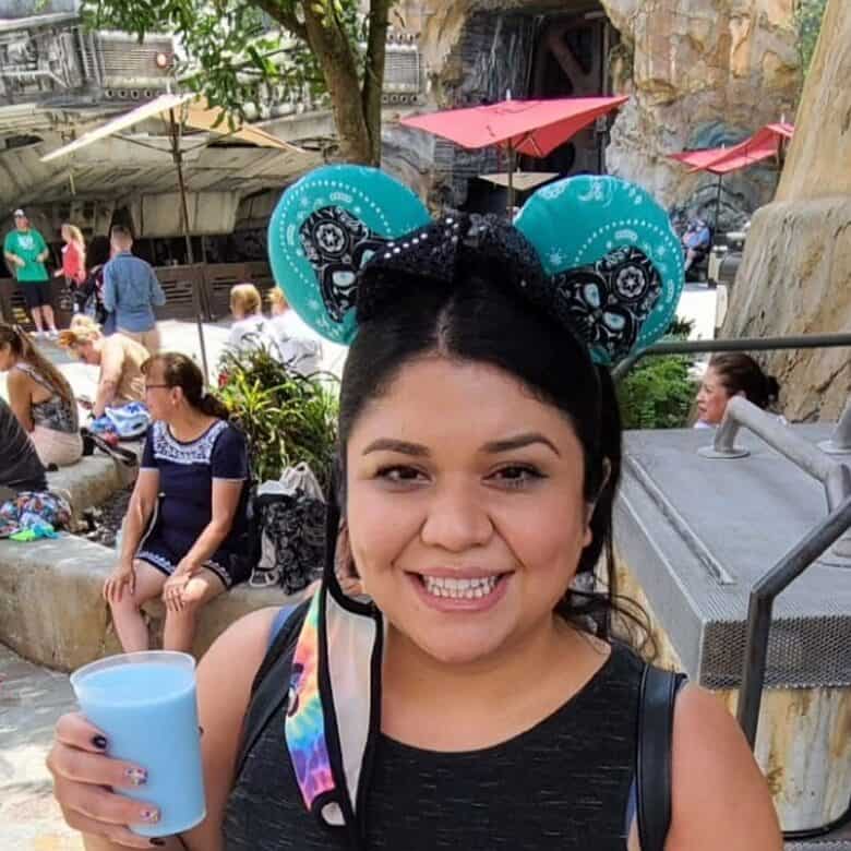 Blue and black Mickey Mouse ears with Dia de los Muertos sugar skull designs, woman smiling at an amusement park.