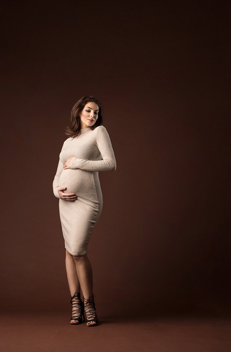 Kvinne med gravid mage i beige kjole og høye hæler, fotografering for gravidfoto, vakkert og stemningsfullt morskapspor, profesjonell gravidfoto, kunstnerisk og personlig bildestudio.