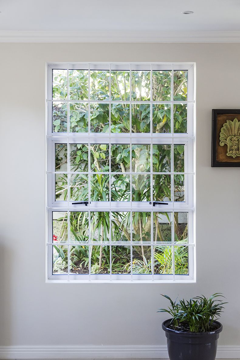 Interior view of pristine white cottage-pane window bars looking onto lush green garden foliage.