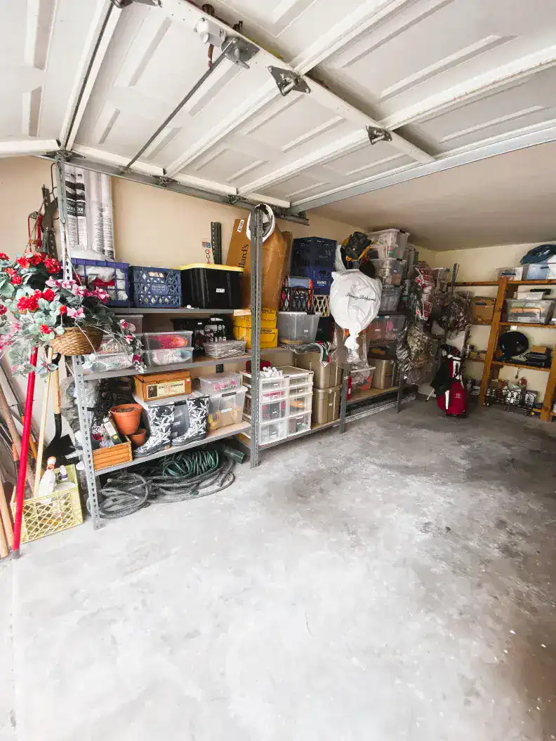 Cluttered garage storage with organized shelves containing tools, gardening supplies, and storage bins.