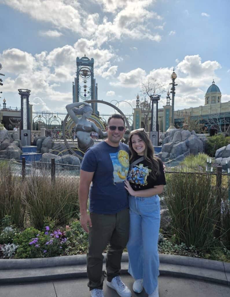 Happy couple at Disney theme park with rides and attractions in background.