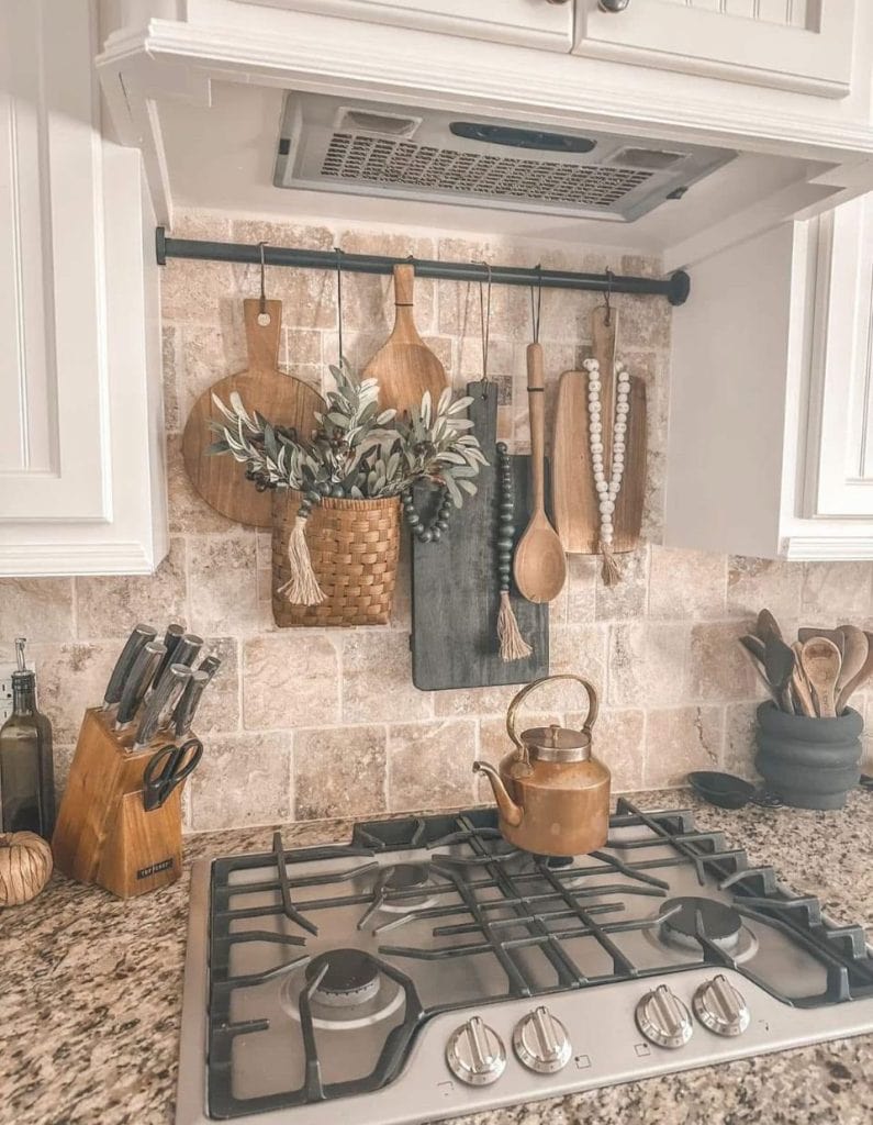 Gas stove top styled with brass and wooden accents and denim colors for a rustic farmhouse touch with wooden cutting boards hanging on the backsplash — charming top of stove decor ideas from By Paige Nicole.