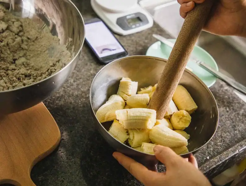 Mãos a misturar a banana com a massa para um pão de banana fofo e saudável.