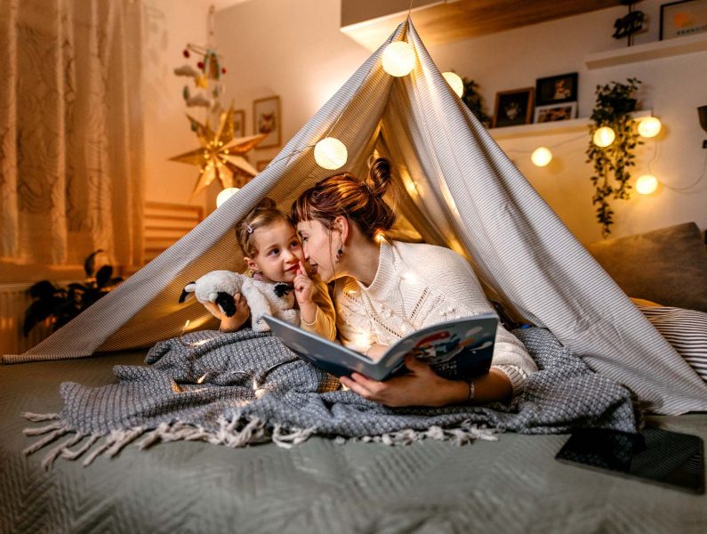 Mãe e filha a ler um livro numa tenda improvisada em casa