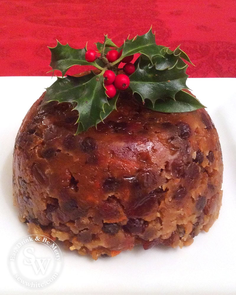 English Traditional Christmas pudding on a white plate with a sprig of holly on top. 