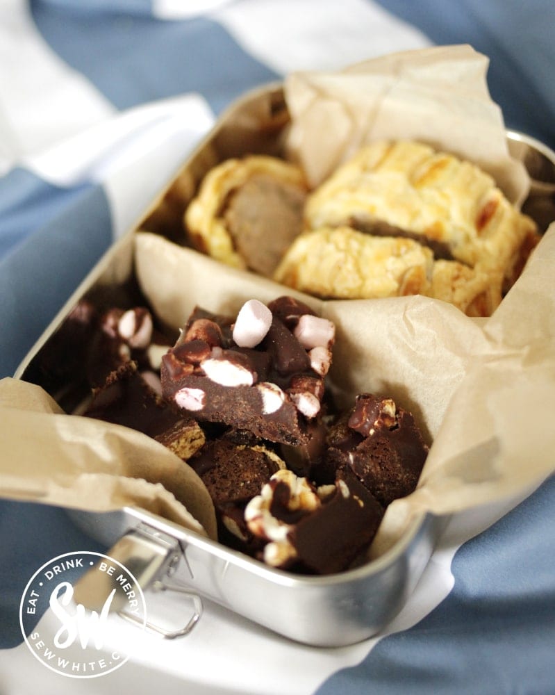 metal lunch box filled with sausage rolls and chocolate baked cake