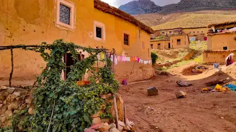 A mountain village in Morocco featuring a dirt road and a traditional house, promoting local travel experiences.