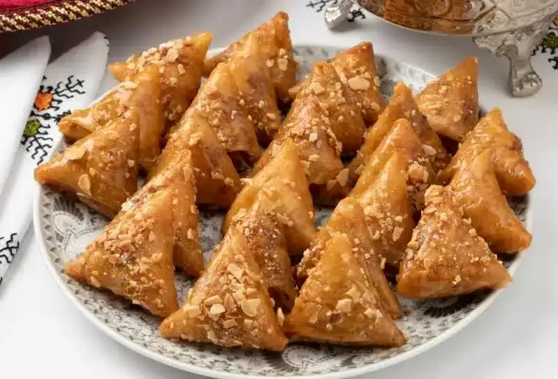 A plate featuring traditional Moroccan sweets alongside a bowl of rice, showcasing vibrant colors and intricate designs.