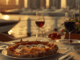 Italienische restaurants in Dubai - auf einem gedeckten Tisch steht ein Teller mit Pizza und ein Glas mit Wein. Im Hintergrund sind der Hafen und Botte zu sehen.